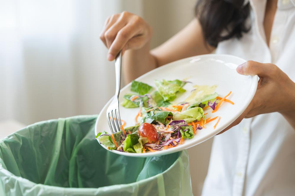 a person scraping food waste off a plate into the trash bin